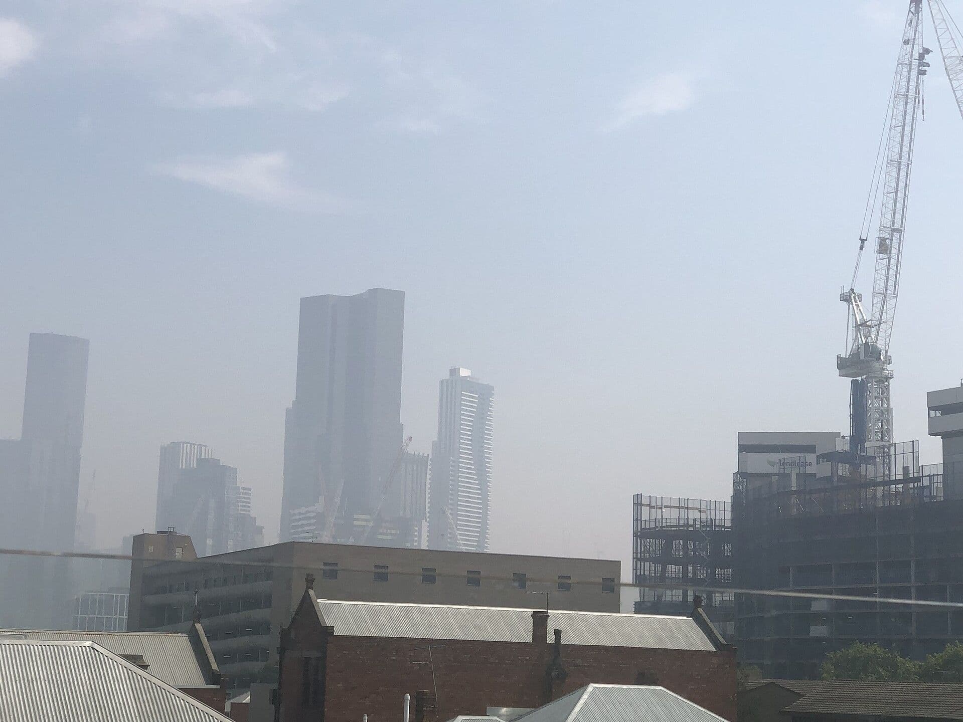 City towers and a crane standing in haze above older brick rooftops.