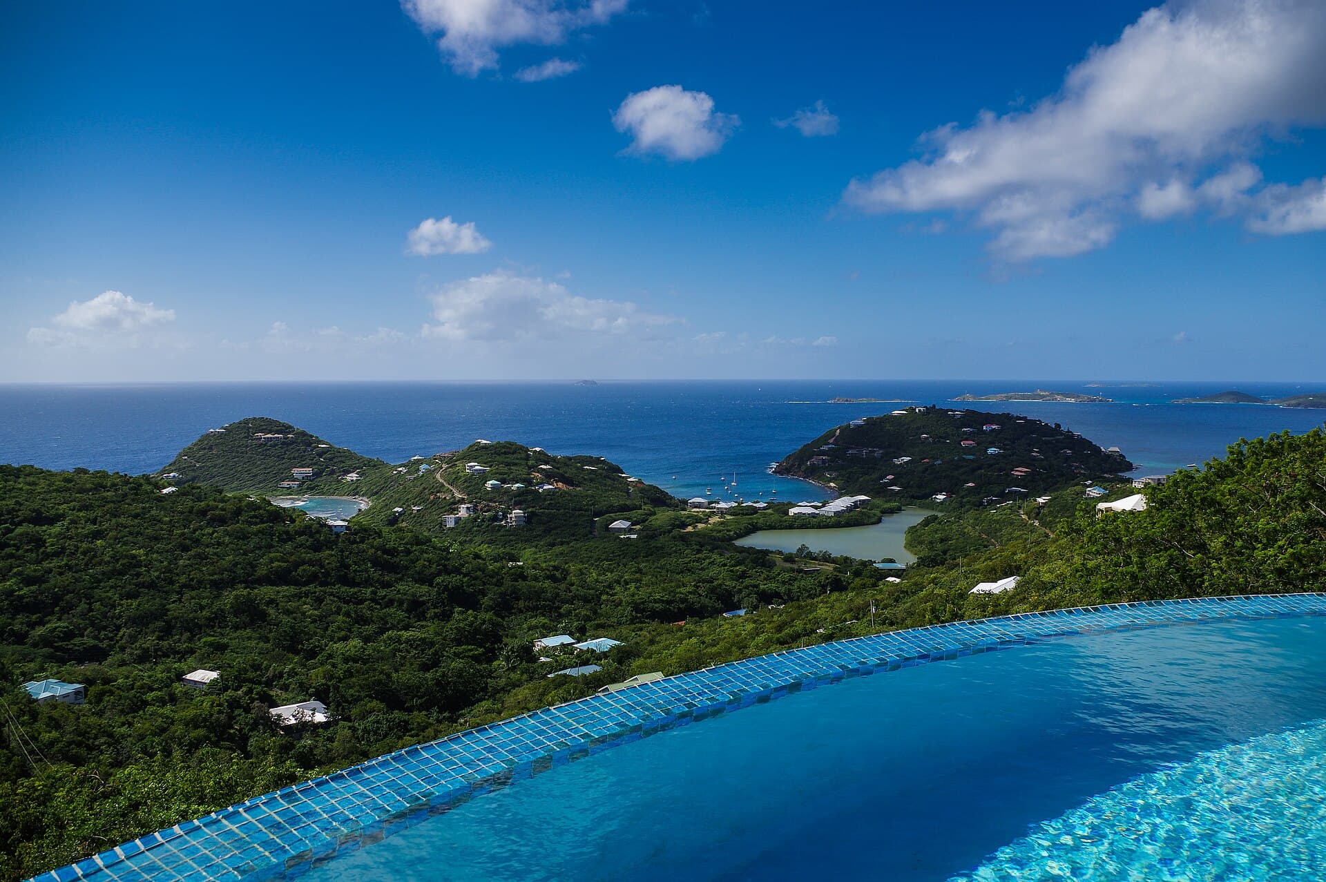 A curved infinity pool above green hills and a blue bay with islands.