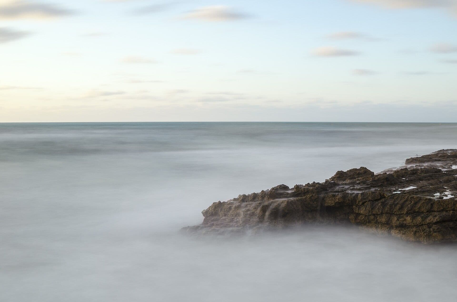 Calm sea in soft light, with a rock shelf in the foreground.